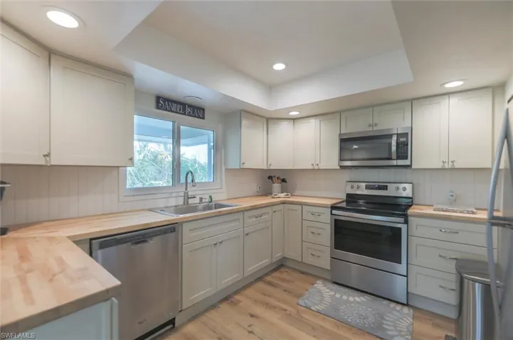 Kitchen featuring light hardwood / wood-style floors, sink, butcher block counters, a raised ceiling, and appliances with stainless steel finishes