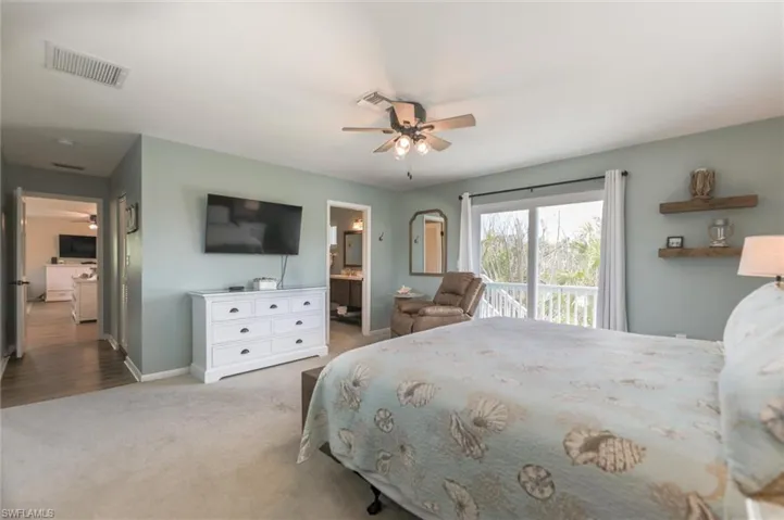 Carpeted bedroom with ceiling fan, ensuite bathroom, and access to exterior
