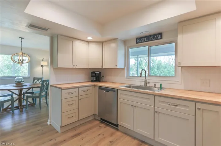 Kitchen featuring hanging light fixtures, dishwasher, wooden counters, sink, and a chandelier