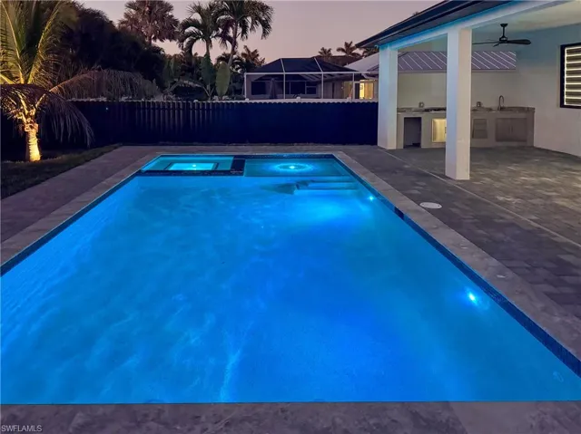 Pool at dusk featuring a patio area, ceiling fan, and an outdoor kitchen