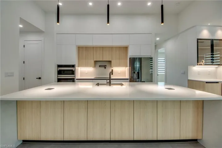 Kitchen with a large island, sink, appliances with stainless steel finishes, a high ceiling, and light brown cabinets