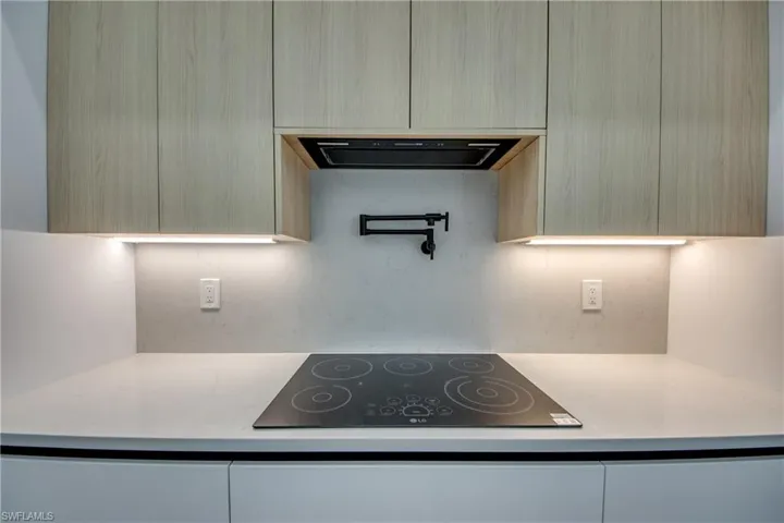 Kitchen with black electric stovetop, light brown cabinetry, and range hood