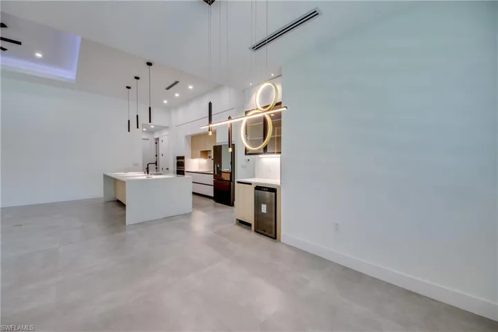 Kitchen featuring stainless steel refrigerator with ice dispenser, wine cooler, sink, a center island with sink, and pendant lighting