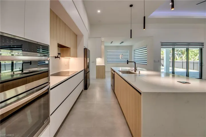 Kitchen featuring appliances with stainless steel finishes, decorative light fixtures, white cabinetry, sink, and a kitchen island with sink