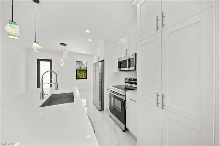 Kitchen featuring light marble finish flooring, appliances with stainless steel finishes, white cabinets, decorative light fixtures, and light countertops