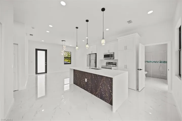 Kitchen with light marble finish flooring, white cabinetry, a kitchen island with sink, appliances with stainless steel finishes, and recessed lighting