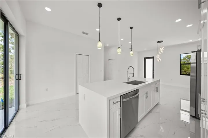Kitchen featuring light marble finish floors, white cabinets, stainless steel appliances, recessed lighting, and a kitchen island with sink