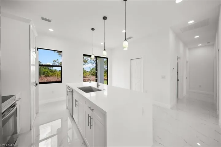 Kitchen with light marble finish flooring, stainless steel appliances, white cabinets, recessed lighting, and an island with sink