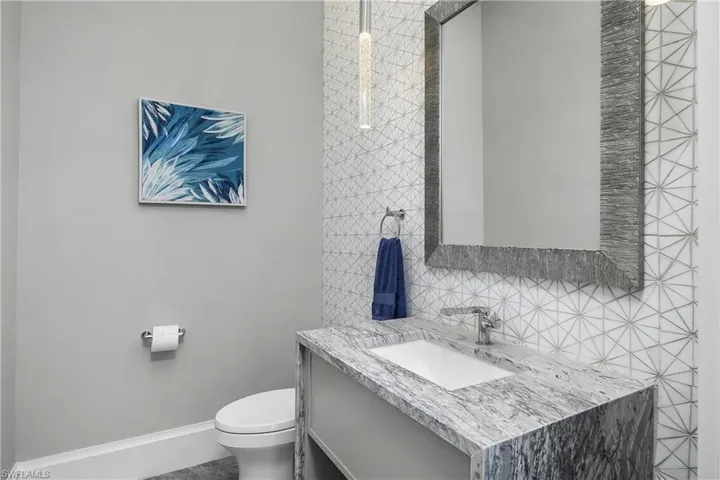 Additional Pool bath located on lanai features leathered quartz countertops, custom tile wall, and designer lighting.