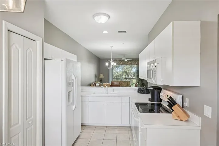 Kitchen with hanging light fixtures, white appliances, light countertops, light tile patterned floors, and white cabinets