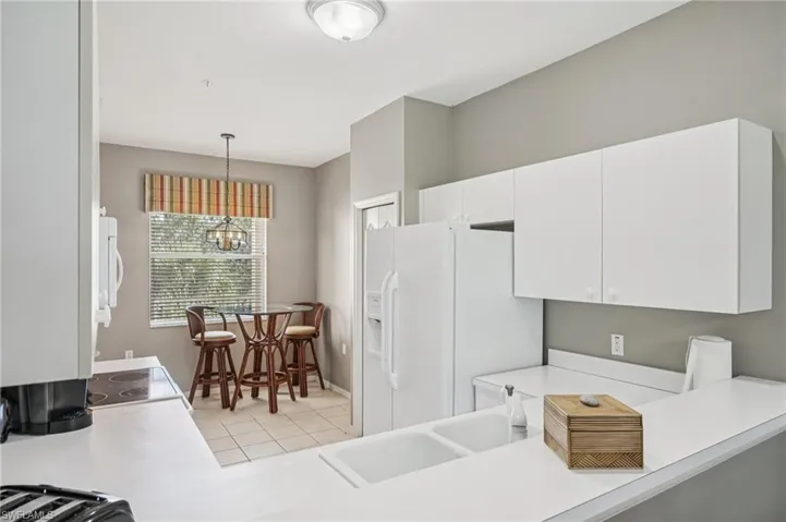 Kitchen featuring light countertops, light tile patterned flooring, decorative light fixtures, white appliances, and white cabinetry