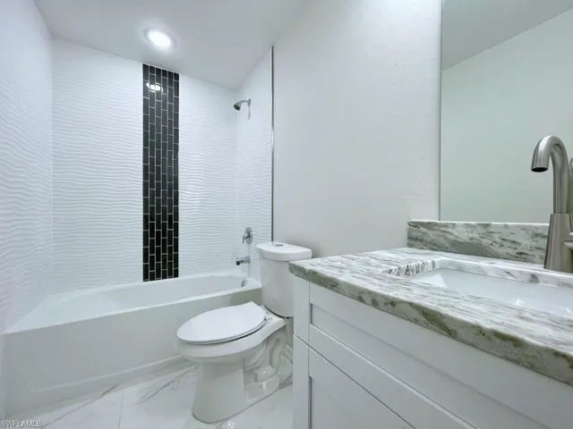 Bathroom with vanity, shower / washtub combination, light marble finish floors, and a textured wall