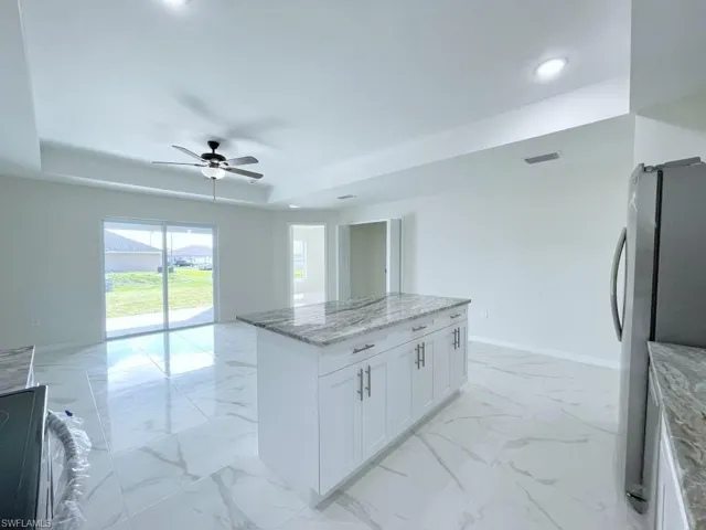 Kitchen featuring light stone counters, freestanding refrigerator, a kitchen island, open floor plan, and ceiling fan