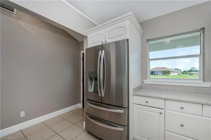 Kitchen with light tile patterned flooring, fridge, and white cabinetry