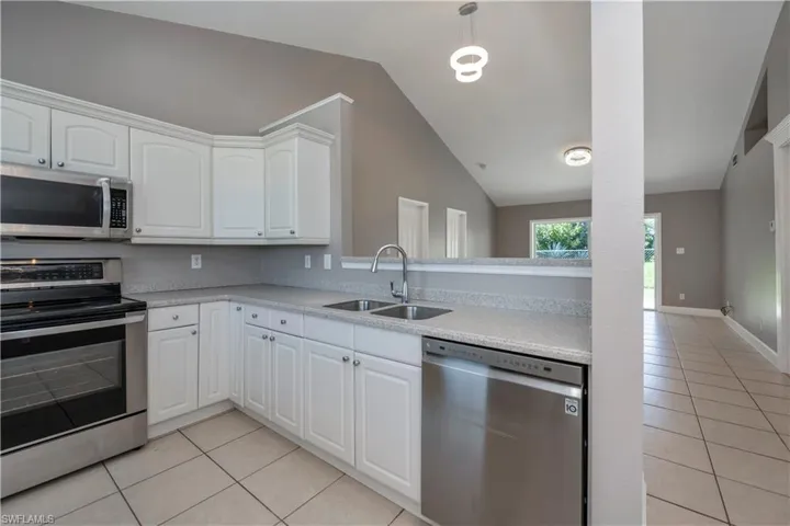 Kitchen featuring white cabinets, appliances with stainless steel finishes, light tile patterned floors, sink, and lofted ceiling