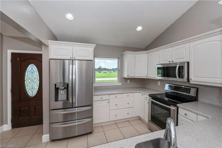 Kitchen featuring appliances with stainless steel finishes, lofted ceiling, white cabinets, and light tile patterned floors