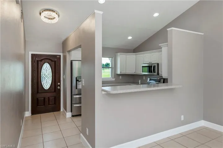 Kitchen with light tile patterned floors, vaulted ceiling, white cabinetry, stainless steel appliances, and kitchen peninsula