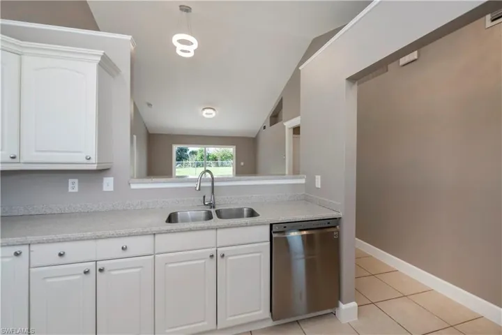 Kitchen with white cabinetry, stainless steel dishwasher, vaulted ceiling, and sink