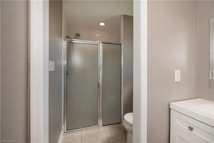 Bathroom featuring a shower with door, toilet, tile patterned floors, and vanity