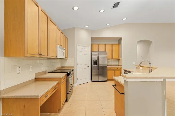 Kitchen featuring light tile patterned flooring, a kitchen island with sink, stainless steel appliances, vaulted ceiling, and decorative backsplash