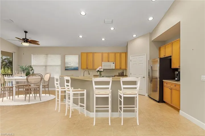 Kitchen featuring a kitchen breakfast bar, stainless steel fridge, light tile patterned flooring, an island with sink, and ceiling fan