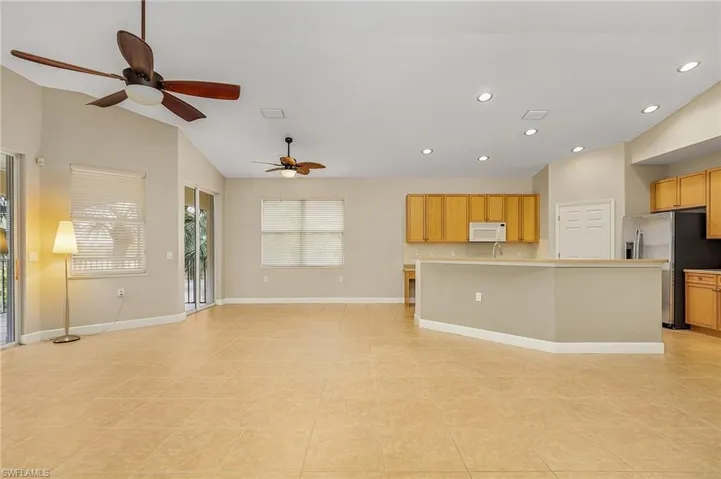 Kitchen with a kitchen island with sink, lofted ceiling, stainless steel refrigerator with ice dispenser, light tile patterned floors, and ceiling fan