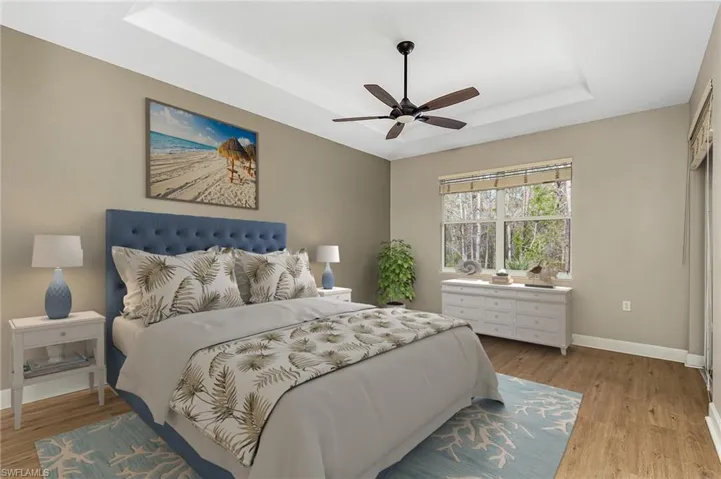 Bedroom with light hardwood / wood-style floors, ceiling fan, and a tray ceiling