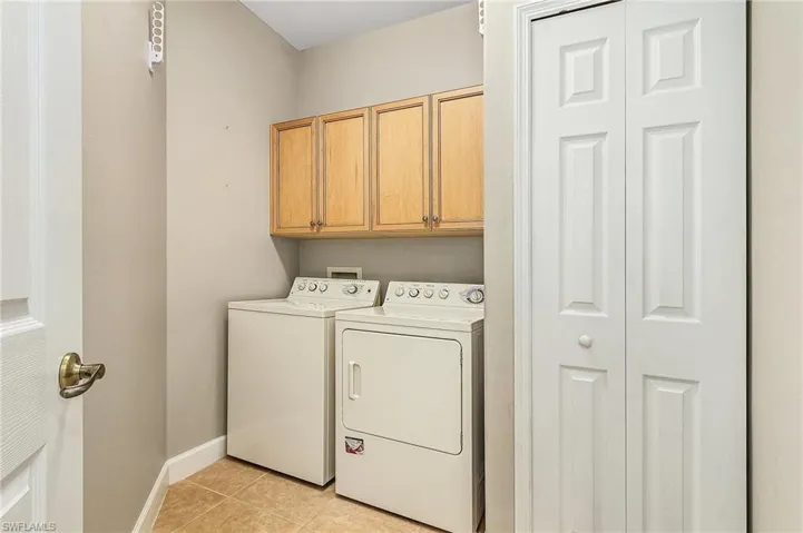 Washroom with washer and clothes dryer, light tile patterned floors, and cabinets