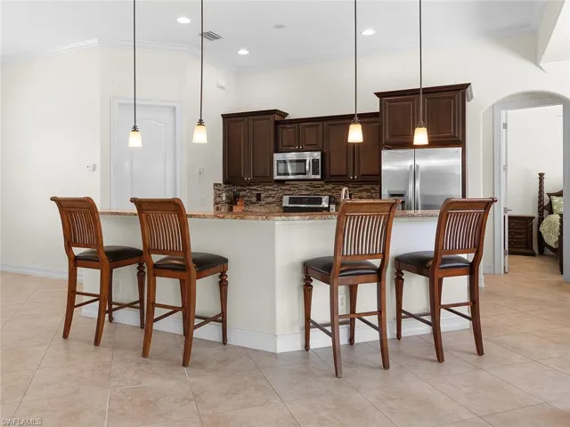 Kitchen with dark brown cabinetry, arched walkways, ornamental molding, a kitchen breakfast bar, and stainless steel appliances