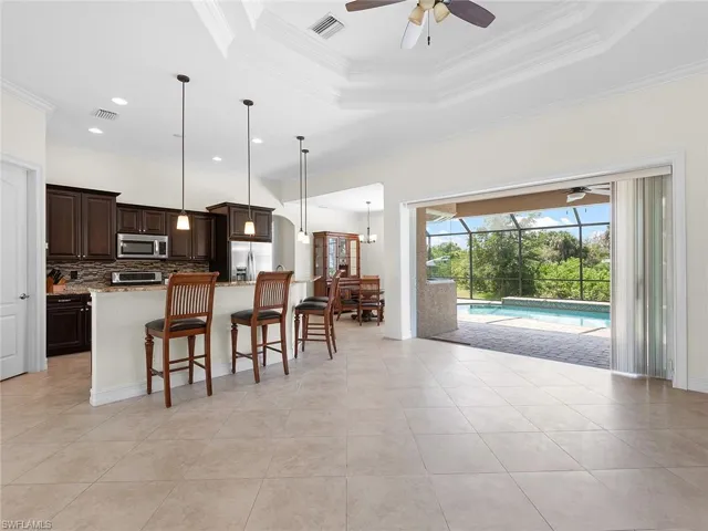 Kitchen with stainless steel appliances, a raised ceiling, visible vents, dark brown cabinets, and a kitchen bar