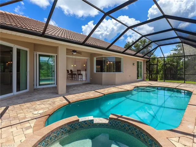 View of swimming pool featuring a ceiling fan, a pool with connected hot tub, glass enclosure, and a patio