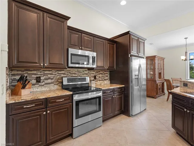 Kitchen featuring ornamental molding, dark brown cabinets, appliances with stainless steel finishes, and tasteful backsplash