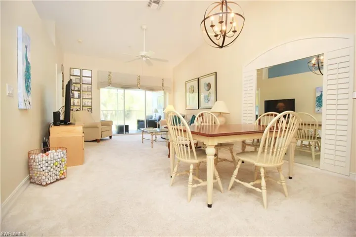 Carpeted dining room featuring ceiling fan with notable chandelier and vaulted ceiling