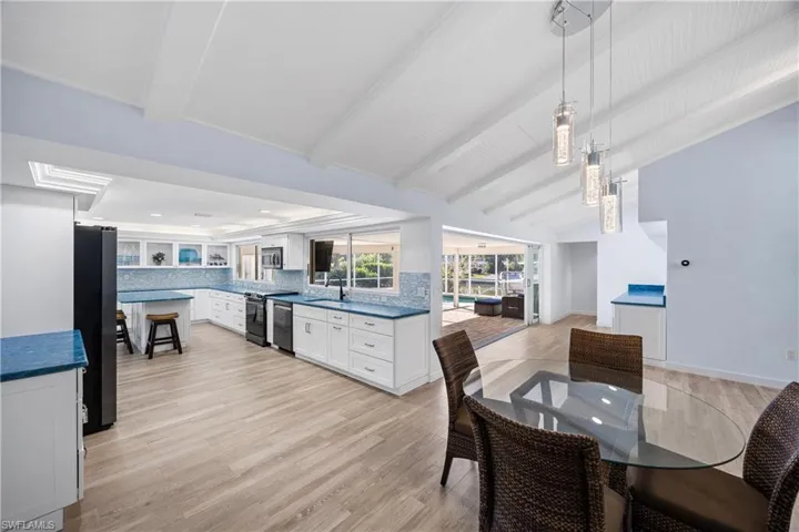 Kitchen with white cabinetry, a kitchen bar, a raised ceiling, black appliances, and light wood finished floors
