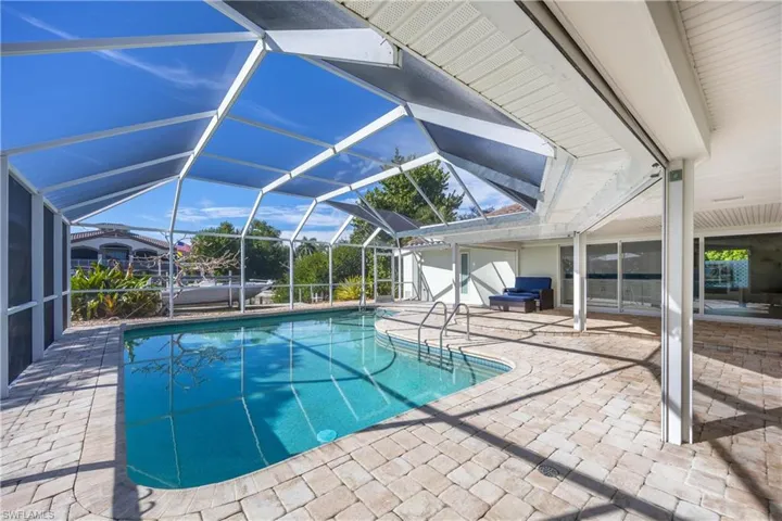 Swimming pool featuring glass enclosure, a patio, and a sunroom