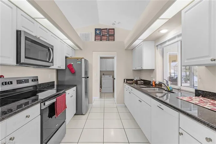 Kitchen featuring dark stone counters, white cabinetry, stainless steel appliances, sink, and lofted ceiling