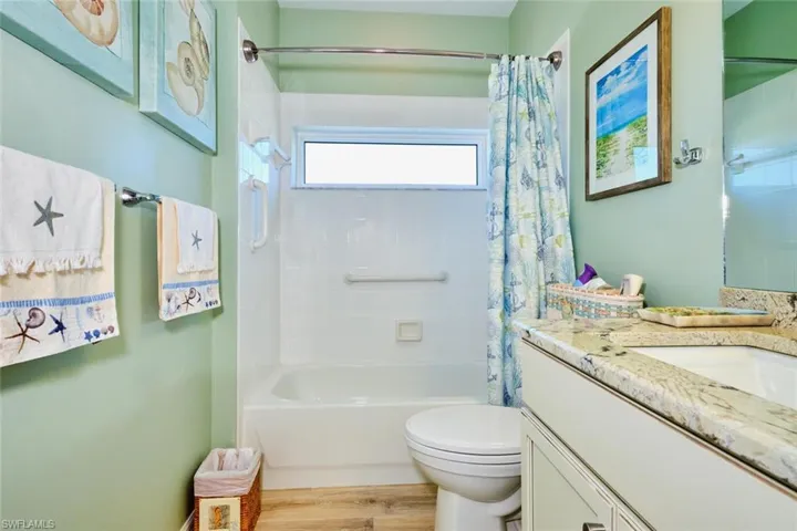 Bathroom with shower / bathtub combination with curtain, toilet, wood finished floors, and vanity
