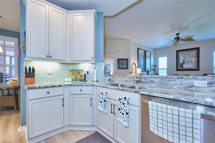 Kitchen featuring backsplash, light stone counters, white cabinets, a ceiling fan, and a sink