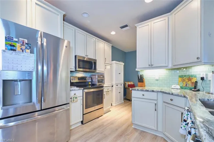 Kitchen featuring visible vents, light stone countertops, decorative backsplash, light wood-style floors, and stainless steel appliances
