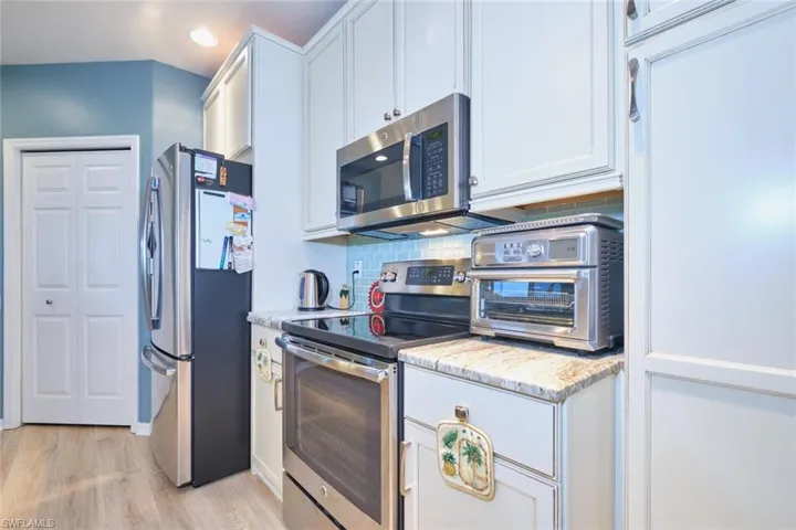 Kitchen featuring decorative backsplash, white cabinetry, light wood-type flooring, and appliances with stainless steel finishes