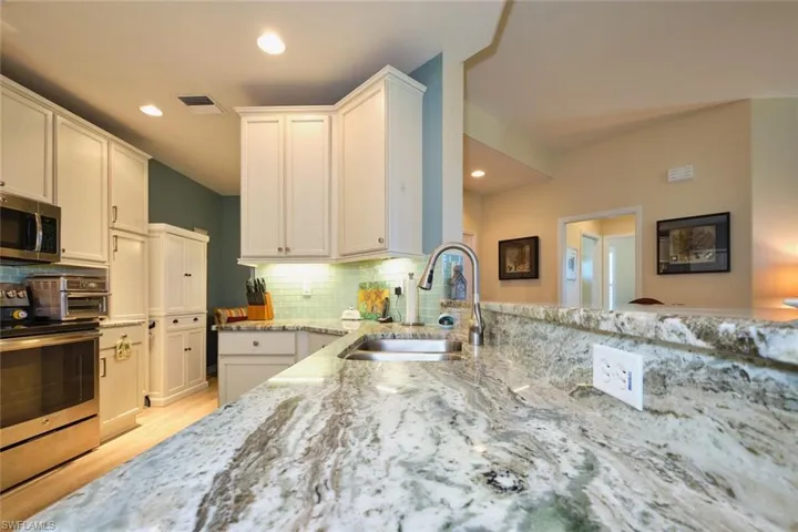 Kitchen with visible vents, backsplash, light stone countertops, stainless steel appliances, and a sink