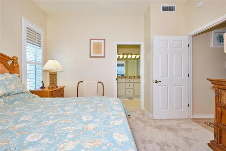 Carpeted bedroom with ensuite bath, baseboards, and visible vents