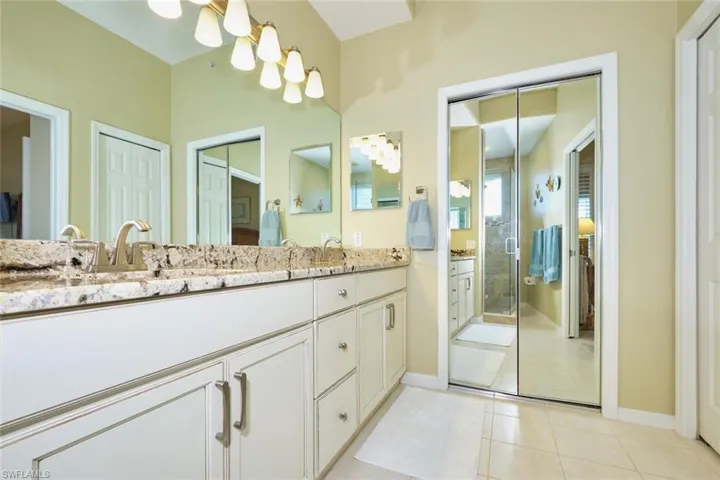 Full bath with tile patterned flooring, a shower stall, baseboards, and double vanity