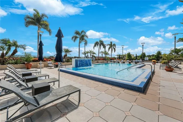 Outdoor pool deck featuring a geometric paver patio, a rectangular swimming pool with a mosaic tile border, and a built-in water feature