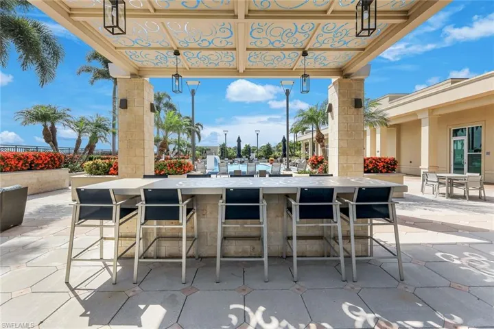 Outdoor entertainment area featuring a stone-clad bar with seating for five, a decorative overhead pergola with pendant lighting, and a patterned paver patio