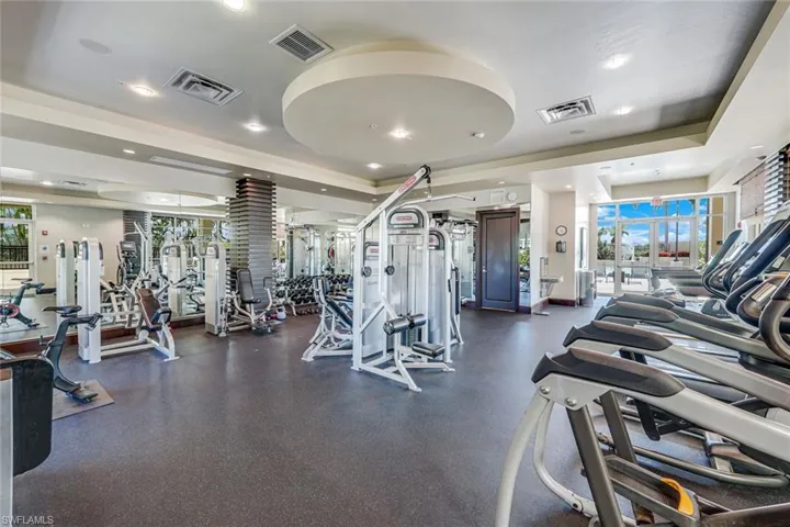 Spacious fitness center featuring rubber flooring, mirrored walls, recessed lighting, and large windows