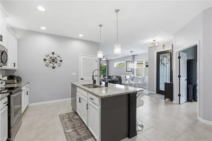 Kitchen featuring an island with a sink, pendant lighting, stainless steel appliances, light-toned cabinetry with dark hardware, and granite countertops