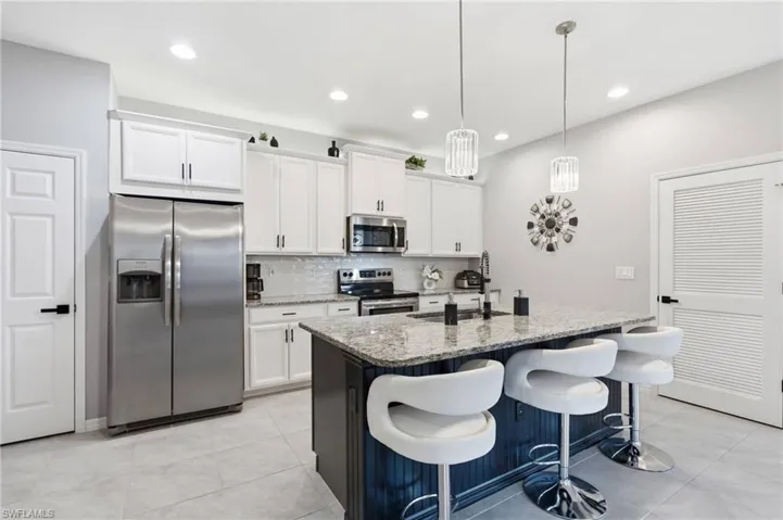 Modern kitchen featuring an island with a light-toned countertop, white cabinetry, integrated stainless steel appliances, a tile backsplash, and recessed lighting