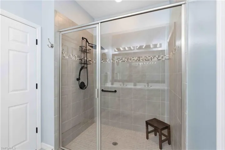 Glass-enclosed shower featuring large format wall tiles, a decorative mosaic tile band, and a textured floor