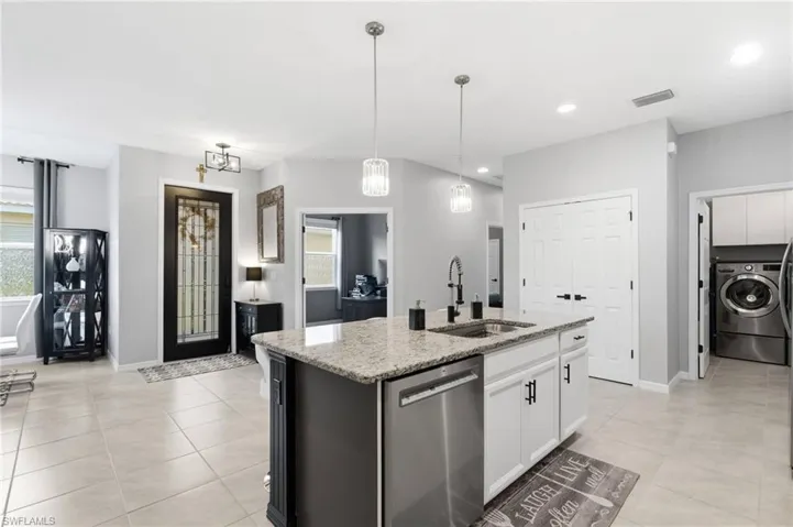 Open-concept kitchen featuring a central island with a granite countertop, built-in sink, and stainless steel dishwasher